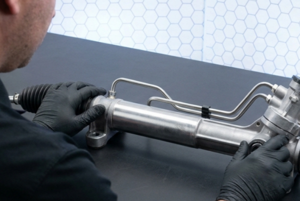 Técnico examinando una cremallera de dirección hidráulica con latiguillos y fuelles sobre una mesa de trabajo.